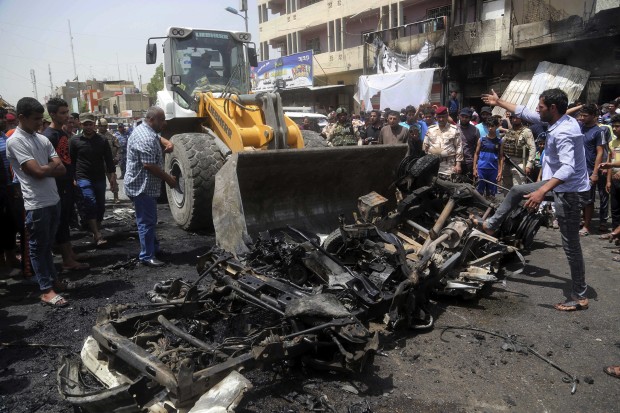 A municipality bulldozer cleans up while citizens inspect the scene after a car bomb explosion at a crowded outdoor market in the Iraqi capital's eastern district of Sadr City, Iraq, Wednesday, May 11, 2016. An explosives-laden car bomb ripped through a commercial area in a predominantly Shiite neighborhood of Baghdad on Wednesday, killing and wounding dozens of civilians, a police official said. (AP Photo/ Khalid Mohammed)