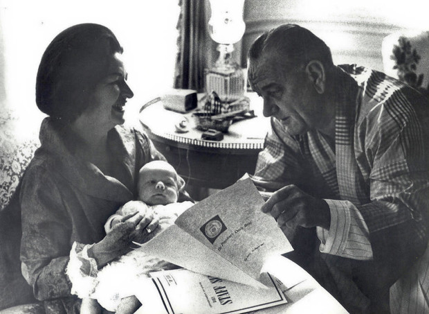 This image provided by the White House shows President Lyndon Johnson reading the President's Daily Brief as his wife Lady Bird Johnson holds their first grandchild in the White House in Washington. AP