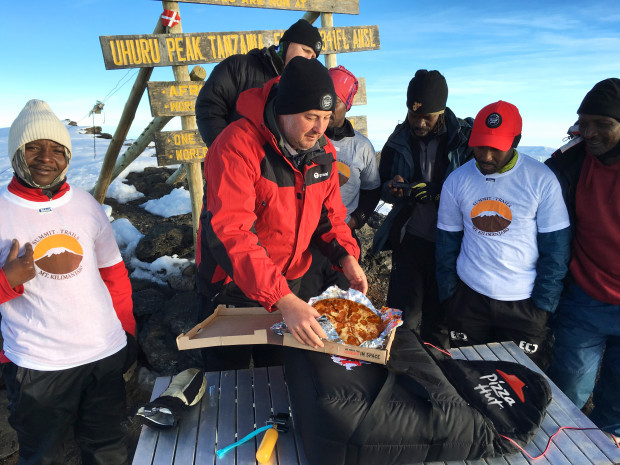 In this Monday, May 9, 2016, photo, provided by Pizza Hut, Pizza Hut Africa General Manager Randall Blackford, center, celebrates setting a world record pizza delivery to the top of Mount Kilimanjaro in Tanzania by offering the team a slice of hot pizza at the summit. With the ascent, Blackford and a team of employees landed the Guinness World Record for the highest altitude pizza delivery. (Consea Dissa/Pizza Hut via AP) MANDATORY CREDIT