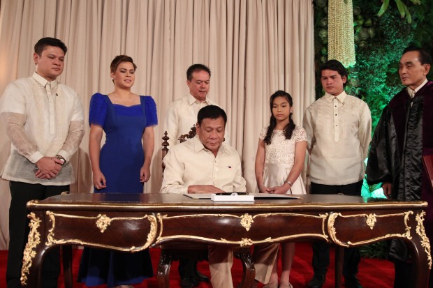President Rodrigo Roa Duterte signs his Oath of Office. Behind him are his children witnessing the signing. MALACAÑANG POOL PHOTO