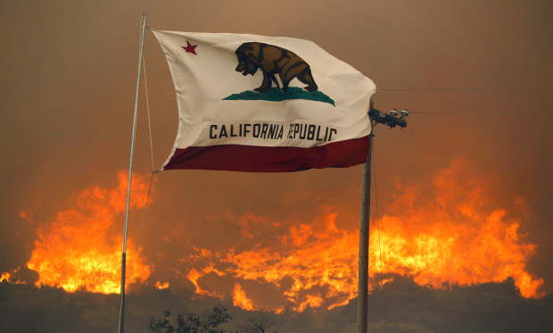 The California state flag flies next to a home on Highway 94 south Potrero, Calif., on Monday, June 20, 2016, as huge flames roar behind it. An intensifying heat wave stretching from the West Coast to New Mexico threatened to make the fight against Southern California wildfires more difficult Monday. (Hayne Palmour IV/San Diego Union-Tribune via AP)