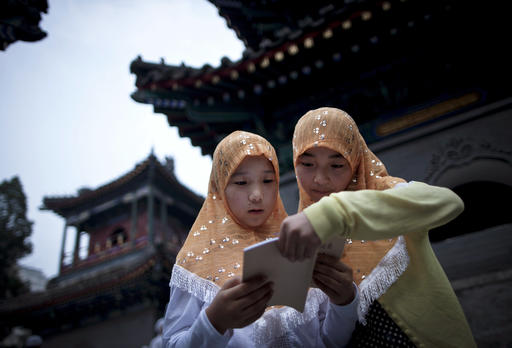 FILE - In this Aug. 1, 2011 file photo, two Chinese Hui Muslim girls read the Quran, Islam's holy book, at the Niujie Mosque as they wait for their fast on the first day of the Muslim holy month of Ramadan in Beijing. A heavily Muslim Chinese province has demanded strict adherence to a ban on religion in schools after a video circulated online in which a kindergartener recites verses from the Quran. (AP Photo/Andy Wong, File)