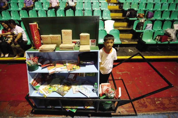 An alumnus of DepEd’s “Kariton’’ program stands next to his mobile classroom, a pushcart loaded with storybooks and other educational materials, during Thursday’s graduation rites in Pasig City. PHOTO BY RAFFY LERMA