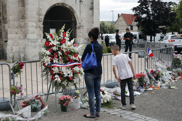 People gather to pay respect with flowers and candles next to the church where an hostage taking left a priest dead the day before in Saint-Etienne-du-Rouvray, Normandy, France, Wednesday, July 27, 2016. The Islamic State group crossed a new threshold Tuesday in its war against the West, as two of its followers targeted a church in Normandy, slitting the throat of an elderly priest celebrating Mass and using hostages as human shields before being shot by police. (AP Photo/Francois Mori)