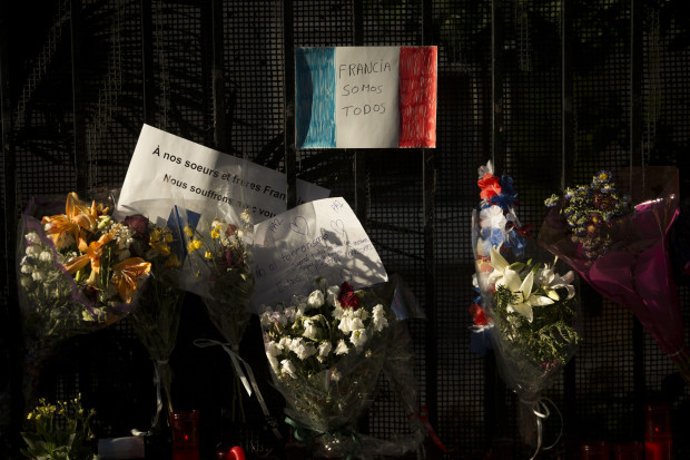 A sheet of paper with the colors of the French flag reading "We are all France" in Spanish, hangs among flowers outside the French embassy in Madrid, Saturday, July 16, 2016. As new details emerged Friday about the Tunisian man who drove a truck through crowds celebrating Bastille Day in Nice, killing at least 80 people and wounding hundreds others, French leaders extended a state of emergency imposed after the Nov. 13 Paris attacks and vowed to deploy thousands of police reservists on the streets. (AP Photo/Francisco Seco)