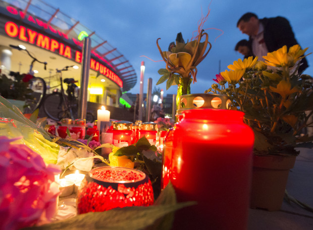People gather to read tributes among the flowers and candles near to the Olympia shopping center where a shooting took place leaving nine people dead the day before in Munich, Germany, Saturday, July 23, 2016. Police piecing together a profile of the gunman whose rampage at a Munich mall Friday left nine people dead described him Saturday as a lone, depression-plagued teenager. (AP Photo/Jens Meyer)