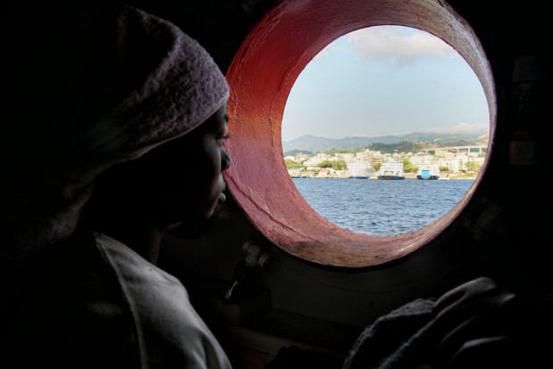 FILE - In this Saturday June 25, 2016 file photo, a woman looks out of the porthole from aboard the 'Aquarius' rescue vessel after arriving in Sicily, Italy with more than 600 migrants aboard the ship rescued by SOS Mediterranee and the medical aid group Medecins Sans Frontieres (MSF). By trying to prevent migrants from taking the dangerous sea journey across the Mediterranean, they are dooming them to prolonged abuse in Libya at the hands of authorities and the country’s many militias, rights groups warn. (AP Photo/Bram Janssen, File)