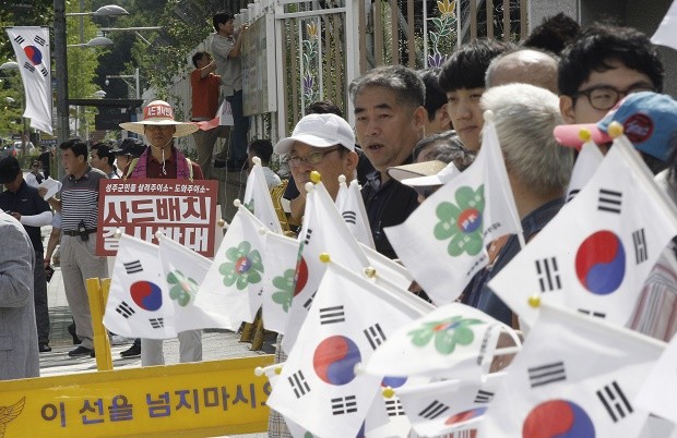 South Korean conservative activists wave the national flags during a rally to support a deployment of the Terminal High-Altitude Area Defense, or THAAD, as an anti-war protester stands in front of the Defense Ministry in Seoul, South Korea, Friday, July 15, 2016. An advanced U.S. missile defense system will be deployed in a rural farming town in southeastern South Korea, Seoul officials announced Wednesday, angering not only North Korea and China but also local residents who fear potential health hazards that they believe the U.S. system might cause. The sign reads "Oppose a deployment of the THAAD." AP 