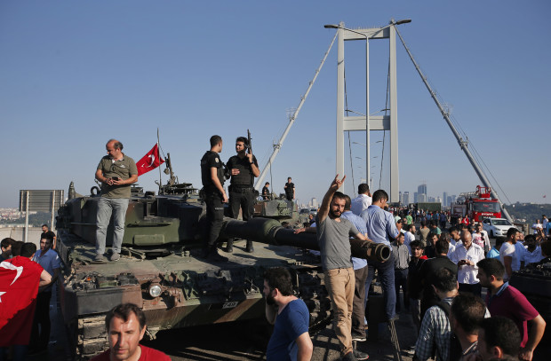 People gather for celebration around Turkish police officers, loyal to the government, standing atop tanks abandoned by Turkish army officers, against a backdrop of Istanbul's iconic Bosporus Bridge, Saturday, July 16, 2016. Turkish President Recep Tayyip Erdogan declared he was in control of the country early Saturday as government forces fought to squash a coup attempt during a night of explosions, air battles and gunfire that left dozens dead. (AP Photo/Emrah Gurel)