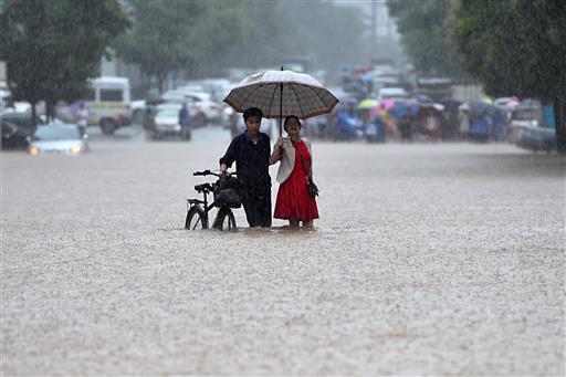 In this Wednesday, July 6, 2016 photo, a couple holding an umbrella in a rain wade through a flooded road in Wuhan in central China's Hubei province. Water levels are starting to recede in central and eastern China Thursday following a week of heavy downpours that have broken levees, flooded cities and villages, halted public transportation, and left at least hundreds people dead or missing. AP