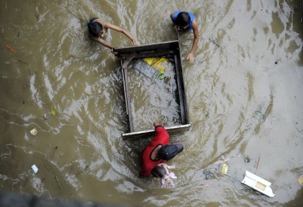 A man (bottom) carries a piglet to higher ground as he wades through a flooded street in San Mateo, Rizal province, east of Manila on August 13, 2016. Floods inundated major thoroughfares in the capital late on August 12, after heavy rains brought about by southwest moonson, authorities said on August 13. / AFP PHOTO / NOEL CELIS
