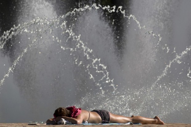 A woman sunbathes next to water fountains in Battersea Park in London on August 23, 2016, as blue skies and warm temperatures sweep the capital. / AFP PHOTO / JUSTIN TALLIS