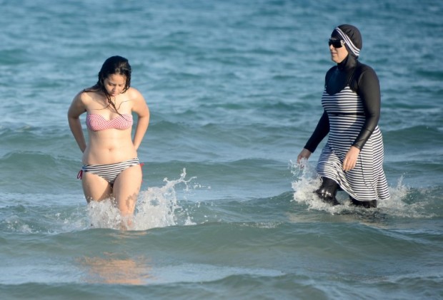 Tunisian women, one (R) wearing a "burkini", a full-body swimsuit designed for Muslim women, swim on August 16, 2016 at Ghar El Melh beach near Bizerte, north-east of the capital Tunis.  / AFP PHOTO / FETHI BELAID