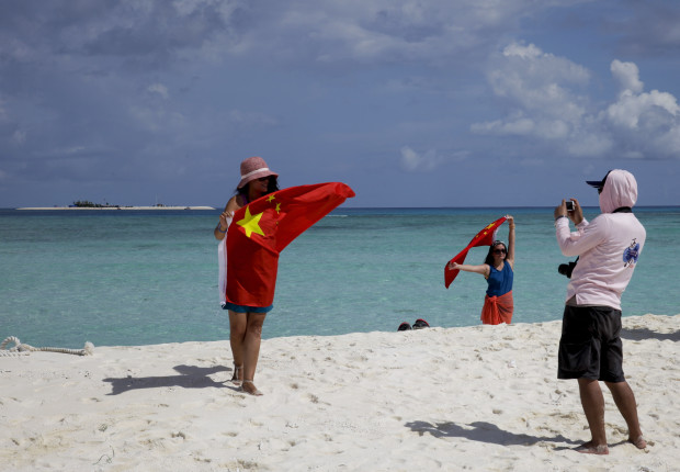 FILE - In this Sept. 14, 2014 file photo, Chinese tourists take souvenir photos with the Chinese national flag as they visit Quanfu Island, one of Paracel Islands of Sansha prefecture of southern China's Hainan province in the South China Sea. Two state-owned companies have announced plans to develop floating nuclear reactors for use by oil rigs or island communities. If they succeed, the achievement would raise concern the reactors might be sent into harm’s way to support oil exploration in the South China Sea, where Beijing faces conflicting territorial claims by neighbors including Vietnam and the Philippines. (AP Photo/Peng Peng, File)