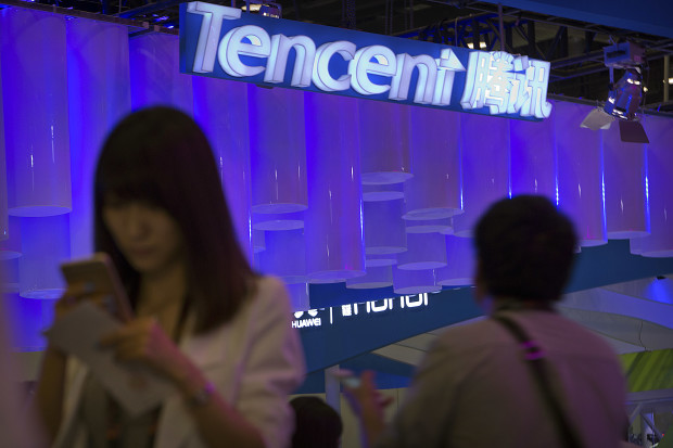 In this April 29, 2015 photo, a woman uses her smartphone near a booth for the Chinese Internet company Tencent at the Global Mobile Internet Conference in Beijing. Chinese state media reported Thursday, Aug. 18, 2016, that new rules hold chief editors of news websites personally liable for content, months after several portals posted material that was seen as embarrassing to President Xi Jinping. Tencent, one of China's most popular websites, fired its top editor after a July headline mistakenly said Xi delivered a "furious" - instead of "important" - speech commemorating a Communist Party anniversary. (AP Photo/Mark Schiefelbein)