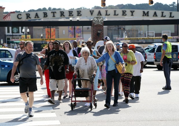 A group of shoppers and workers walk across Glenwood Avenue as Crabtree Valley Mall is evacuated in Raleigh, N.C., Saturday, Aug. 13, 2016. Raleigh's police chief says investigators are still trying to determine whether there was a shooting at the Raleigh mall where witnesses reported hearing gunfire. (Chris Seward/The News & Observer via AP)