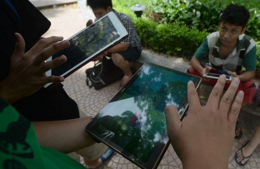 People use tablets and smartphones to play the newly launched Pokemon Go game at a public park next to Hoan Kiem Lake in the centre of Hanoi on August 10, 2016. The game made its debut in the Southeast Asian nation on August 6. / AFP PHOTO / HOANG DINH NAM