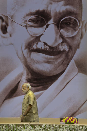 In this April 24, 2015 file photo, Indian Prime Minister Narendra Modi walks past a huge portrait of Mahatma Gandhi during an event to mark the national Panchayati Raj or village civil council day, in New Delhi, India. AP