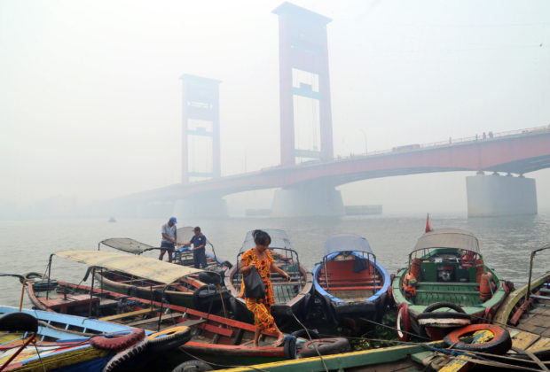 FILE - In this Sept. 29, 2015 file photo, a woman disembarks from a boat as the Ampera Bridge is shrouded in haze from wildfires in Palembang, South Sumatra, Indonesia. Indonesian, Malaysian and Singaporean authorities have dismissed research that smoky haze from catastrophic forest fires in Indonesia last year caused 100,000 deaths. Some even contend the haze caused no serious health problems, but experts say those assertions contradict well-established science. Others say governments should not dismiss the study even if the estimated deaths are arguable. (AP Photo, File)