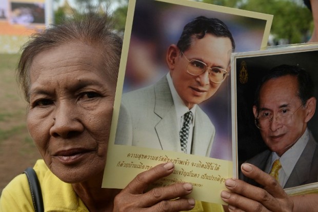 A woman holds up images of Thailand's King Bhumibol Adulyadej to celebrate the 70th anniversary of his reign in Bangkok on June 9, 2016. Thailand marked the 70th anniversary of King Bhumibol's ascension to the throne following the mysterious 1946 death of his brother as anxieties deepen over the increasingly frail health of the hospital-bound monarch. / AFP PHOTO / LILLIAN SUWANRUMPHA