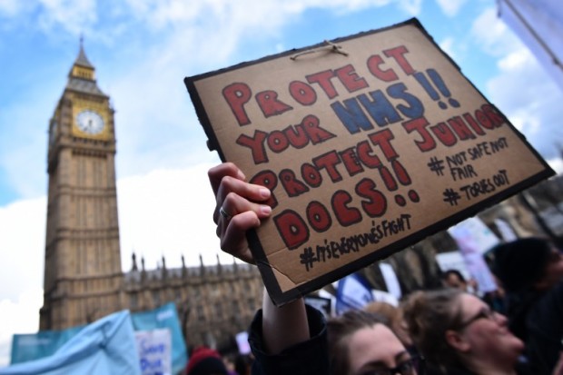 A protester holds a placard reading "protect your NHS, protect junior doctors" during a demonstration by doctors joined by teachers in central London on April 26, 2016 during a junior doctors strike over the imposition of a new contract. Junior doctors in England staged their first ever all-out strike Tuesday in a bitter, deadlocked row with Prime Minister David Cameron's government over pay and conditions. The strike forced 13,000 operations and 113,000 appointments to be postponed by the National Health Service, which employs more than 50,000 junior doctors.  / AFP PHOTO / BEN STANSALL