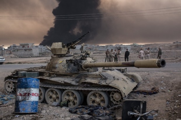 Iraqi soldiers stand next to a tank as smoke rises from the Qayyarah area, some 60 kilometres (35 miles) south of Mosul, on October 19, 2016, during an operation against Islamic State (IS) group jihadists to retake the main hub city. In the biggest Iraqi military operation in years, forces have retaken dozens of villages, mostly south and east of Mosul, and are planning multiple assaults for October 20. / AFP PHOTO / YASIN AKGUL