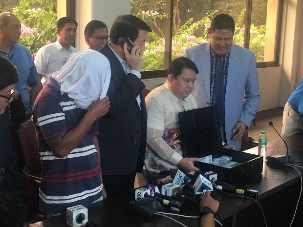 Lawyer Ferdie Topacio (second from right) shows media the P1 million reward for the tipster (with head covered) who led to the arrest of Ronnie Dayan. MARC JAYSON CAYABYAB