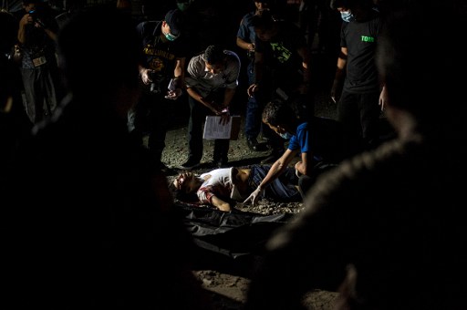 This photo taken on July 27, 2016 shows a police officer investigating the dead body of an alleged drug pusher killed in the street in Manila. Hundreds of people have died since President Rodrigo Duterte won a landslide election in May, promising to rid society of drugs and crime in six months by killing tens of thousands of criminals. Police figures showed this week that 402 drug suspects had been killed a month into Duterte's presidency. This figure does not include those slain by suspected vigilantes. / AFP PHOTO / NOEL CELIS / TO GO WITH Philippines-crime-drugs-rights,FOCUS by Noel Celis