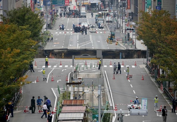 This photo shows a giant sinkhole (C) in a five-lane urban boulevard, eroding soil and exposing underground steel columns supporting commercial buildings in Fukuoka, southwestern Japan, on November 8, 2016.  No injuries were reported as the accident occurred in the early morning hours.      / AFP PHOTO / JIJI PRESS / STR / Japan OUT