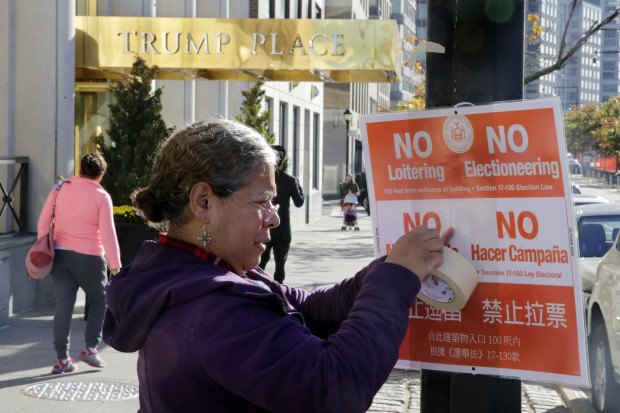 FILE- In this Nov. 8, 2016 file photo, poll interpreter Mayra Mora affixes a sign outside of a polling place in an apartment building named for then Republican presidential candidate Donald Trump, in New York. The luxury apartment building is one of three that will have the president-elect's name stripped from it after hundreds of residents signed an online petition demanding it be removed. (AP Photo/Richard Drew, File)