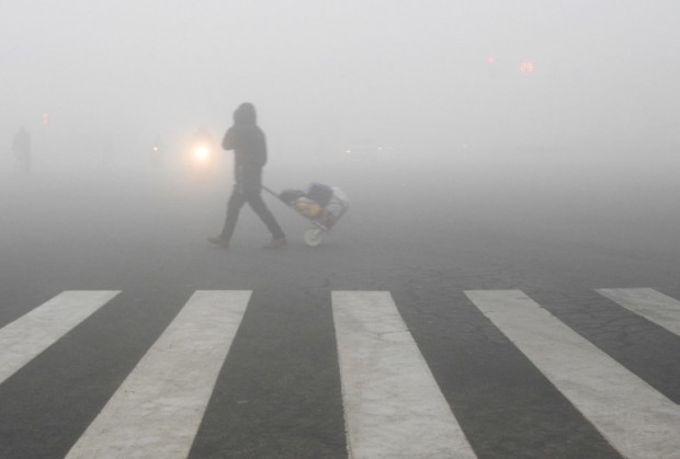 A pedestrian crosses a smog-shrouded street in Lianyungang, eastern China's Jiangsu province on December 19, 2016.  Hospital visits spiked, roads were closed and flights cancelled on December 19 as China choked under a vast cloud of toxic smog, with forecasters warning the worse was yet to come. / AFP PHOTO / STR / China OUT