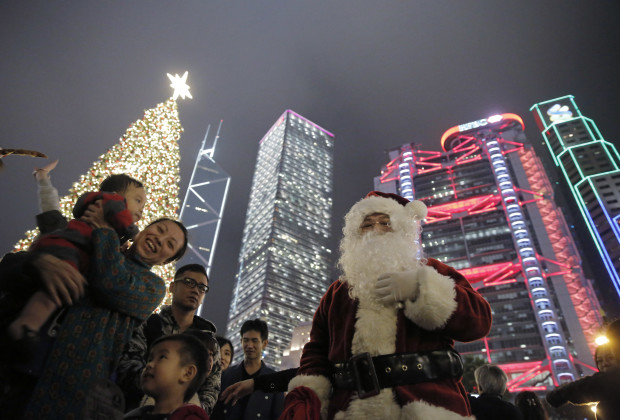 A man dressed as Santa Claus poses for photos in front of a Christmas tree installation during Christmas eve as they celebrate the festival season in Hong Kong, Saturday, Dec. 24, 2016. (AP Photo/Kin Cheung)