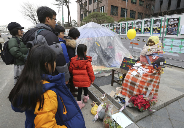 People watch a statue symbolizing women forced into wartime Japanese military brothels in front of the Japanese Embassy in Seoul, South Korea, Sunday, Jan. 8, 2017. A South Korean Buddhist monk is in critical condition after setting himself on fire to protest the country's settlement with Japan on compensation for wartime sex slaves, officials said Sunday. (AP Photo/Ahn Young-joon)
