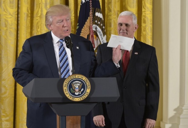 US President Donald Trump holds the letter left for him by former US President Barack Obama, as Vice President Mike Pence watches, before the swearing in of the White House senior staff at the White House on January 22, 2017, in Washington, DC. / AFP PHOTO / MANDEL NGAN