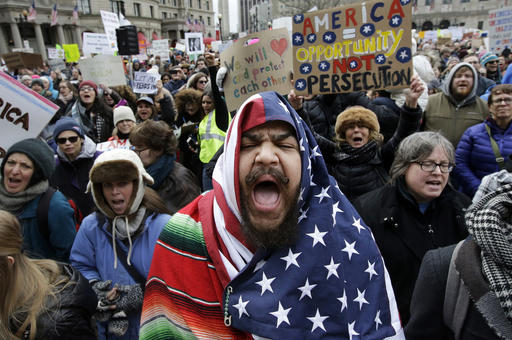 Izzy Berdan, of Boston, center, wears an American flags as he chants slogans with other demonstrators during a rally against President Donald Trump's order that restricts travel to the U.S., Sunday, Jan. 29, 2017, in Boston. Trump signed an executive order Friday, Jan. 27, 2017 that bans legal U.S. residents and visa-holders from seven Muslim-majority nations from entering the U.S. for 90 days and puts an indefinite hold on a program resettling Syrian refugees. (AP Photo/Steven Senne)
