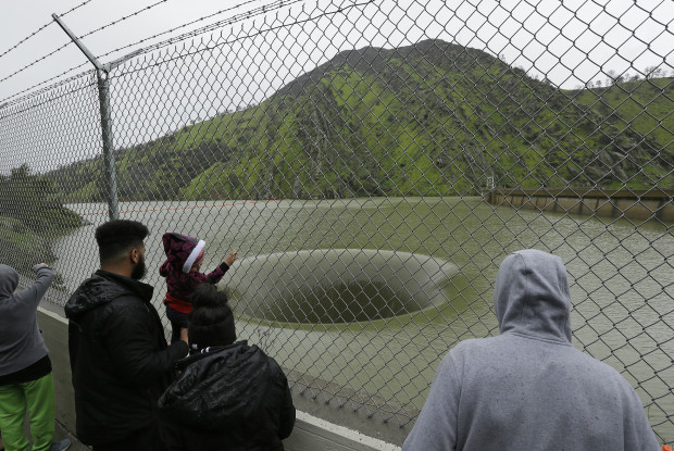 People stop to watch water flow into the iconic Glory Hole spillway at the Monticello Dam on Monday, Feb. 20, 2017, in Lake Berryessa, Calif. Water is flowing for the first time in over a decade into the 72-foot diameter hole due to the recent storms in California. The unique spillway operates similarly to a bathtub drain. Heavy downpours are swelling creeks and rivers and bringing threats of flooding in California's already soggy northern and central regions. The National Weather Service map shows floods, snow and wind advisories for the northern part of the state. (AP Photo/Eric Risberg)