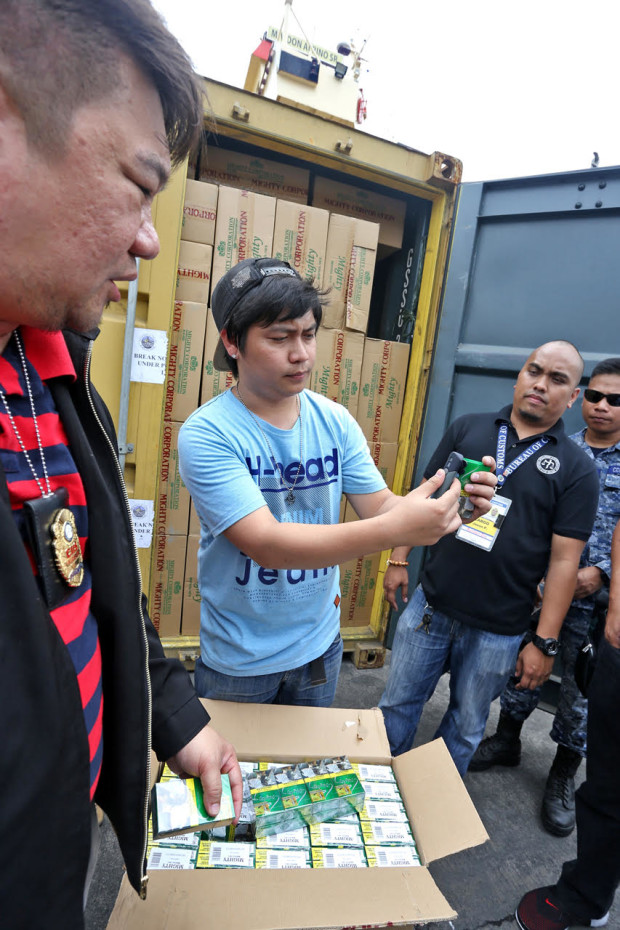 SMUGGLE CIGARETTES/MARCH 7, 2017: Neil Estrella (left) CIIS director of the Bureau of Customs watches as a BIR employee uses a taggant reader to the alledge smuggled Mighty cigarettes pack to confirm that the stamps were fake after it was sized in two. 20 footer container vans at pier 4.(JUNJIE MENDOZA)