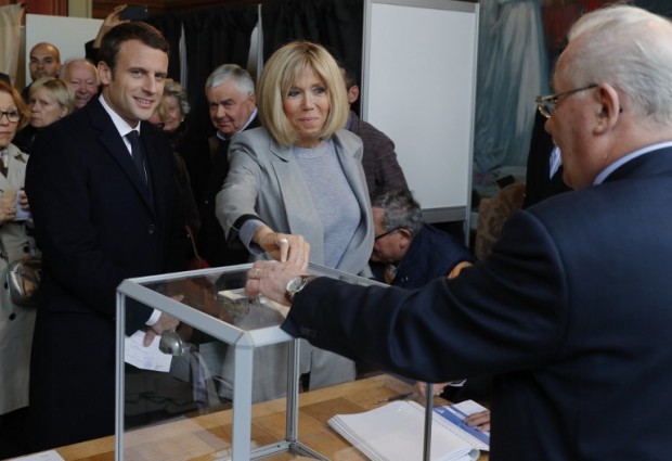 French presidential election candidate for the En Marche ! movement Emmanuel Macron (L) stands next to his wife, Brigitte Trogneux as she casts her ballot at a polling station in Le Touquet, northern France, on April 23, 2017, during the first round of the Presidential election.  / AFP PHOTO / POOL / PHILIPPE WOJAZER