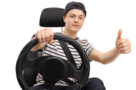 72501308 - teenager seated in a car seat holding a steering wheel and giving a thumb up isolated on white background