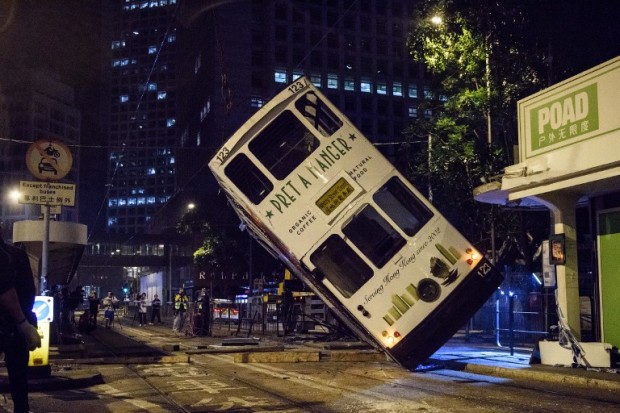 Emergency service personnel and journalists (back) watch as a double-decker tram is lifted by crane after it tipped over on a main road in Hong Kong, early on April 6, 2017. At least eleven people were injured when a double-decker tram tipped over in Hong Kong, authorities said on April 6, in a rare accident on the city's public transport network. Trams, known as "ding-dings" for the sound of their bells, have serviced the city's main island for more than a century and carry around 200,000 passengers a day.  / AFP PHOTO / ANTHONY WALLACE