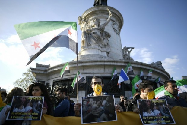Protesters hold pictures and Syria's former independence flags (which have been adopted by the rebels forces fighting against Syrian pro-government forces in Syria) during a demonstration to protest against chemical attacks in Syria on April 6, 2017 on the Place de la Republique, in Paris, two days after a suspected chemical attack in the northwestern province of Idlib. An air strike on rebel-held Khan Sheikhun in Idlib's province on April 4, 2017 left scores of civilians dead from a suspected chemical weapons attack. At least 86 people -- among them 27 children -- were killed, with results from post-mortems performed on victims pointing to possible exposure to sarin, according to Turkish health officials. / AFP PHOTO / Lionel BONAVENTURE