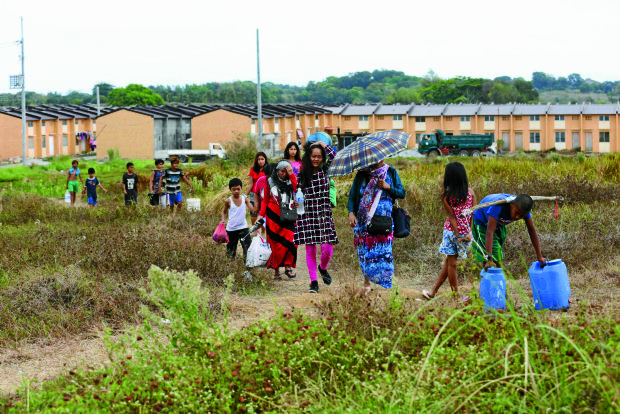 Homeless families belonging to Kadamay cross an open field to their new shelters in Village 2 of Atlantica housing project in Pandi town, Bulacan province. JOAN BONDOC/INQUIRER FILE PHOTO