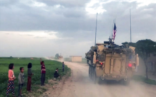 This Friday, April 28, 2017 frame grab from video, shows Syrian children waving as U.S. forces patrol on a rural road in the village of Darbasiyah, in northern Syria. U.S. armored vehicles are deploying in areas in northern Syria along the tense border with Turkey, a few days after a Turkish airstrike that killed 20 U.S.-backed Kurdish fighters, a Syrian war monitor and Kurdish activists said Friday. (AP Photo via APTV)