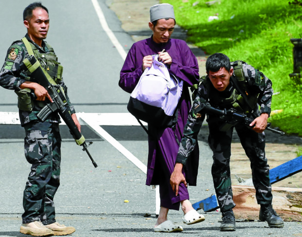 CHECKPOINT Soldiers frisk aMuslim man at a checkpoint near Marawi City. Authorities have been verifying the identities of people in key cities in Mindanao after President Duterte proclaimed martial law on the island in thewake of clashes between government security forces and terrorists linked to the Islamic State group. —BULLITMARQUEZ/AP