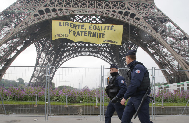 Police officers walk past the Eiffel tower as Greenpeace activists display a banner who reads, 'liberty, equality, fraternity" in Paris, France, Friday, May 5, 2017. The protest is against far-right presidential candidate Marine Le Pen two days before the runoff. (AP Photo/Michel Euler)