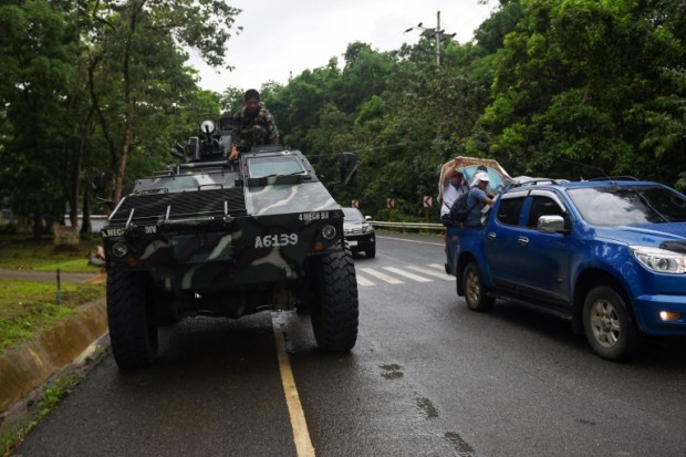 A Philippine soldier sits on an Armoured Personnel Carrier (APC) while residents fleeing from Marawi city drive past on a highway going to Marawi, in Balo-i town, in southern island of Mindanao on May 24, 2017. Islamist militants who triggered martial law in the southern Philippines when they rampaged through a city are threatening to kill a priest and other hostages, the Catholic Church said May 24. / AFP PHOTO / TED ALJIBE