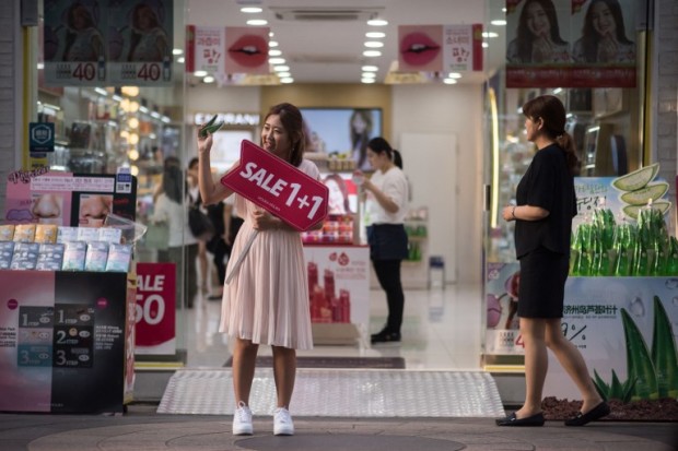 This photo taken on May 18, 2017 shows a salesperson advertising a sale in front of a cosmetics store in the popular Myeongdong shopping area of Seoul. China's boycott of South Korea over a US anti-missile shield on the Korean peninsula shows it is becoming more aggressive in the way it flexes its economic muscles, analyst say. Beijing has banned Chinese tour groups from going to the South, hammering its tourist market and the duty-free shops of retail giant Lotte, which has been targeted for providing land for the controversial defence system.    / AFP PHOTO / Ed JONES / TO GO WITH China-economy-politics-SKorea-Taiwan, FOCUS by Allison JACKSON