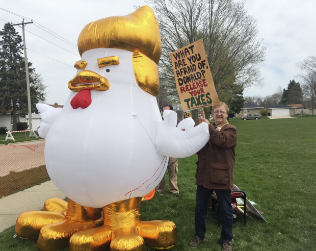 Retired high school teacher Tom Gilding holds a sign as he stands next to an inflated chicken made to resemble President Donald Trump on Tuesday, April 18, 2017, during a protest ahead of Trump's visit to Snap-On Inc. in Kenosha, Wis. (AP Photo/Ivan Moreno)