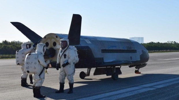 Technicians in space suits stand beside the X-37B spacecraft. US AIR FORCE PHOTO