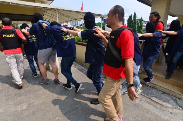 Indonesian police guard men arrested in a recent raid during a press conference at a police station in Jakarta on May 22, 2017.  Indonesian police have detained 141 men who were allegedly holding a gay party at a sauna, an official said on May 22, the latest sign of a backlash against homosexuals in the Muslim-majority country. / AFP PHOTO / FERNANDO